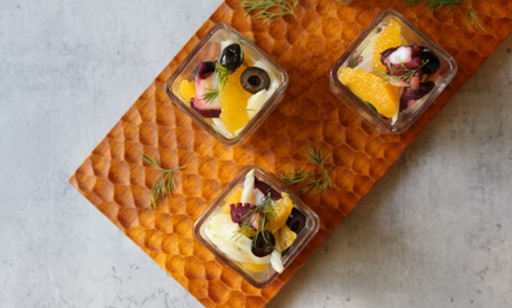 ガラス容器に盛りつけたタコとオレンジのハーブマリネ。カラフルで爽やかな見た目の冷製前菜。